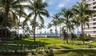 Manicured lawn featuring mature palm trees, multi-level hardscaped walkways with metal railings, and a skyline backdrop