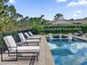Outdoor swimming pool with built-in tanning ledge, raised spillway spa, neutral-toned paved pool deck, and metal perimeter fencing