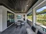 Covered terrace featuring dark wood-plank ceiling, large-format tile flooring, recessed lighting, ceiling fan, and black metal railing