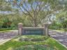 Brick monument signage featuring stone accents, surrounded by mature trees, landscaping, and paved roadway access
