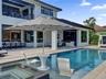 Swimming pool featuring a sun shelf with a built-in table, integrated spa, covered patio, and outdoor kitchen