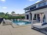 Backyard featuring a rectangular swimming pool, integrated shallow sun shelf, expansive stone-finish decking, and a covered lanai