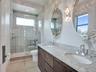 Dual-sink vanity with stone-finish countertop and wood-finish cabinetry, paired with a glass-enclosed shower featuring tile surrounds and wall-mounted