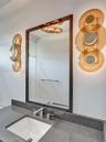 Dark stone countertop with an integrated undermount sink, sleek metal widespread faucet, framed wall mirror, and custom tiered amber glass wall-mounte