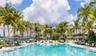 Swimming pool with metal handrails, surrounding stone-finish decking, and mature palm trees