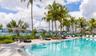 Swimming pool featuring a sun shelf, paved pool deck, and mature palm trees