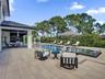 Expansive paved patio with a covered outdoor kitchen, rectangular swimming pool, raised spa, and black metal perimeter fencing