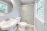 Bright, modern bathroom featuring a pedestal sink with brushed-nickel fixtures, a round mirror, and a frosted glass shower enclosure with decorative e