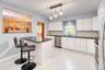 Bright, open kitchen featuring white shaker cabinets, black granite countertops, and a stylish mosaic tile backsplash. A large center island with seat