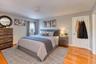 Inviting primary bedroom featuring warm hardwood floors, soft gray walls, and abundant natural light. The space includes a plush area rug, modern wood