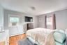 Bright and comfortable bedroom featuring hardwood floors, soft gray walls, and large windows that fill the space with natural light. The room includes