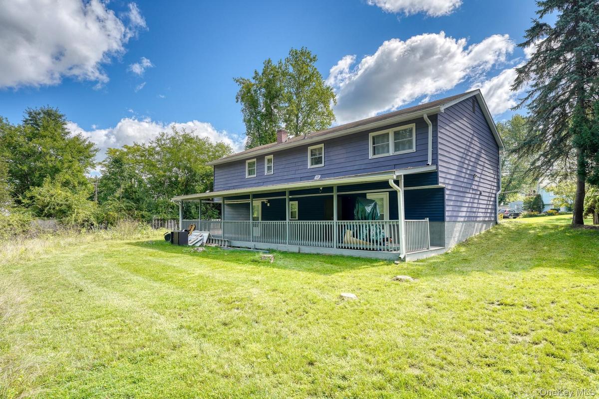 Beautiful outdoor setting showcasing a spacious lawn and a two-story home with a full-length covered porch. The blue exterior contrasts elegantly with