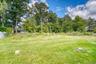 Peaceful backyard view featuring a lush green lawn bordered by mature trees and natural foliage. The wooded backdrop provides privacy and a serene atm