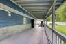 Expansive covered back porch with light gray decking and sturdy railing, offering a shaded retreat overlooking the backyard. The blue siding and expos