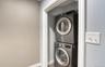 Compact and efficient laundry nook featuring a modern stacked washer and dryer set in a recessed space with clean white trim. The sleek metallic finis