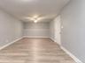 Spacious finished room featuring light gray walls, wide-plank vinyl flooring, and crisp white trim for a clean, modern look. The ceiling fan with inte