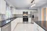 Contemporary kitchen showcasing sleek white cabinetry, stainless-steel appliances, and a polished black granite countertop. The mosaic tile backsplash