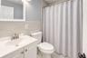 Modern full bath featuring a white vanity with brushed-nickel fixtures, matching hardware, and a sleek integrated sink. Light gray tile walls and floo
