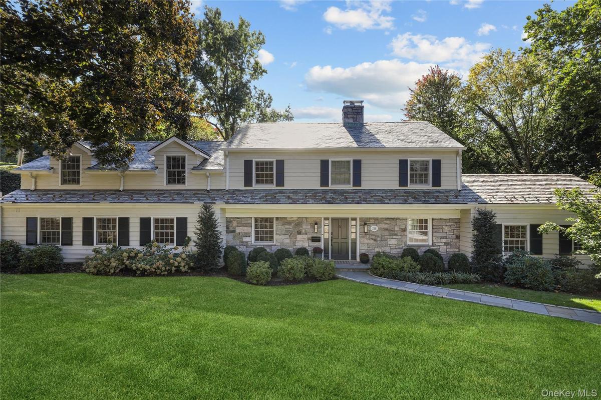 Expansive green lawn, stone and siding facade, multiple dormer windows, slate-style roofing, and mature landscaping