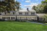 Expansive green lawn, stone and siding facade, multiple dormer windows, slate-style roofing, and mature landscaping