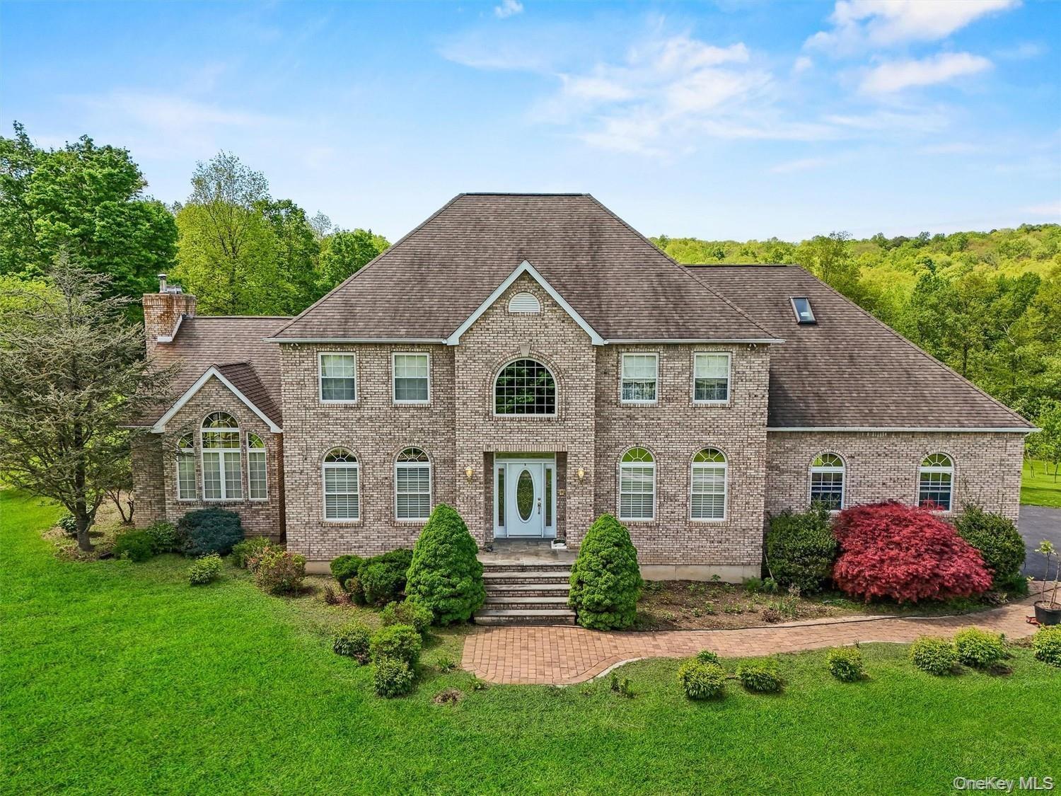 Colonial-style house with brick siding, a chimney, a front lawn, and roof with shingles