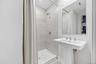 Basement Full Bathroom. Pedestal sink with chrome fixtures, a framed mirror, and a shower with light-toned wall tile