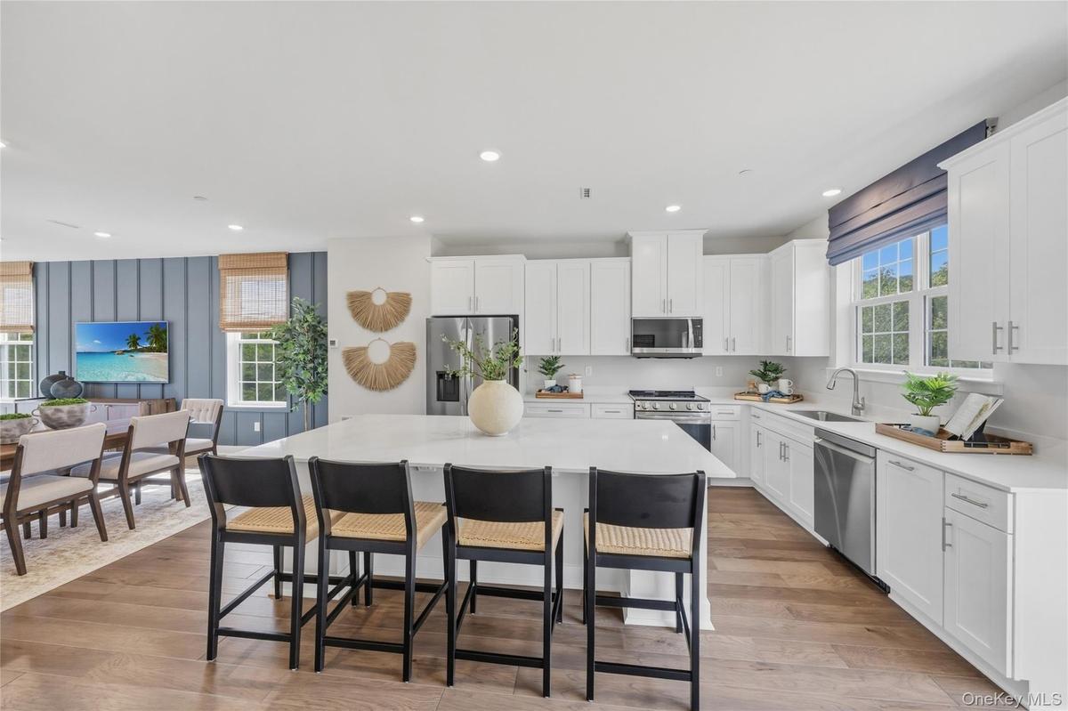 Open-concept kitchen featuring an spacious island with seating, white shaker cabinetry, stainless steel appliances, and wood-finish flooring