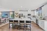 Open-concept kitchen featuring an spacious island with seating, white shaker cabinetry, stainless steel appliances, and wood-finish flooring