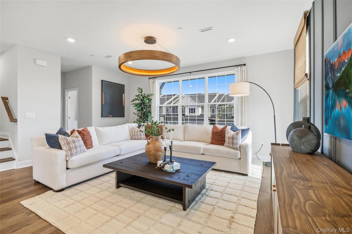 Spacious living area featuring large windows, wood-finish flooring and  recessed lighting.