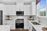 Modern kitchen featuring white shaker cabinetry, stainless steel appliances, light-toned countertops, and a stainless steel sink with a gooseneck fauc