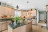 Kitchen with light wood finish cabinetry, a kitchen island with sink, dark stone countertops, hanging light fixtures, and stainless steel appliances