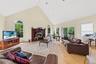 Living room with a high ceiling, light wood-type flooring, a ceiling fan, a premium fireplace, and a baseboard heating unit