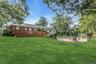 Back of house featuring an outdoor pool, a yard, brick siding, a wooden deck, and a patio area