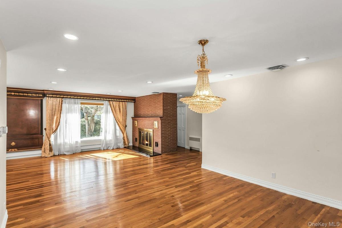 Unfurnished living room with wood finished floors, a fireplace, recessed lighting, radiator, and a chandelier