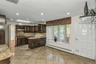 Kitchen featuring glass insert cabinets, dark brown cabinets, baseboard heating, light stone countertops, and decorative backsplash