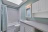 Main Hall Bathroom featuring a skylight, white tile shower surround, integrated vanity sink, and white cabinetry with brushed nickel hardware