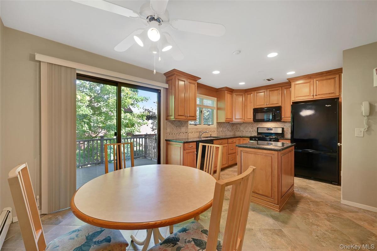 Kitchen featuring wood cabinetry, black appliances, tile flooring, and a sliding glass door to an outdoor deck