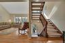 Vaulted ceiling in the living room, wood-finish flooring, large windows, two-story staircase with wood handrails, and a side elongated window by front