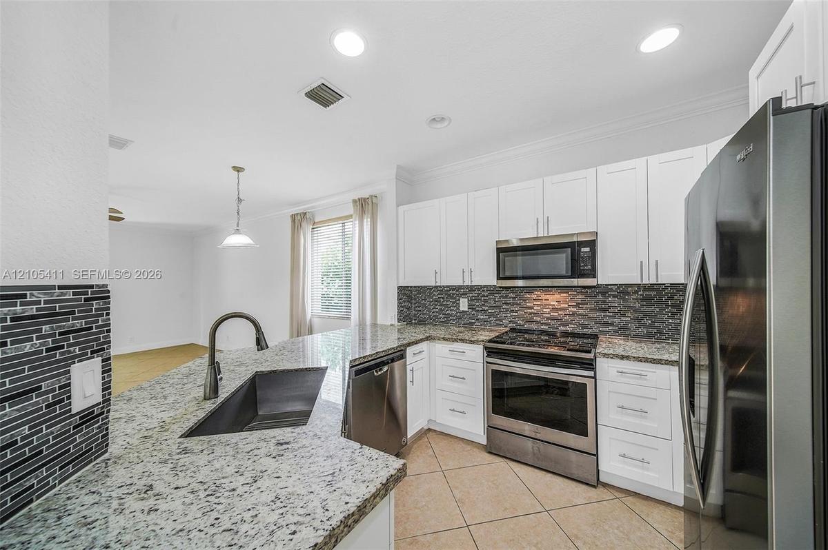Kitchen featuring white cabinetry, stainless steel appliances, granite countertops, and a tiled backsplash