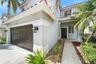 Tiled roof with white gutters, wood-paneled garage door, exterior wall sconces, tiled entryway path, and mature landscaping