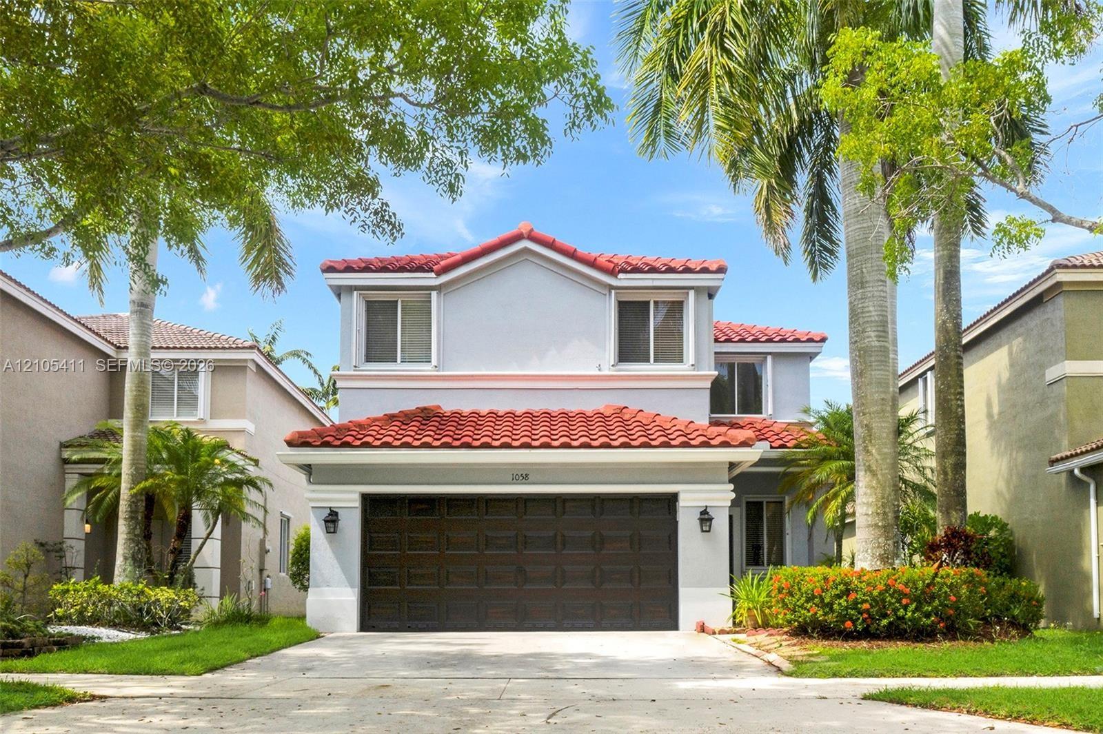Two-story stucco exterior with a red barrel tile roof, integrated garage, and manicured landscaping