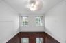 Rich wood-finish flooring, two large windows with blinds, ceiling fan, crown molding, and white textured walls