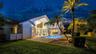 Expansive backyard featuring a manicured lawn, a swimming pool with a surrounding patio, mature palm trees, and a privacy fence