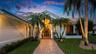 Paver walkway leading to a grand entry, surrounded by mature palm trees, a well-maintained lawn, and stucco exterior with a tile roof