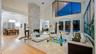 Soaring ceilings with transom windows, stone fireplace, light-toned tile flooring, and French doors opening to an exterior area with a pool