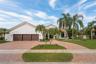 Stucco exterior with a tile roof, three-car garage, brick paver driveway, mature palm trees, and a landscaped lawn