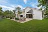 Expansive green lawn, mature palm trees, tiled roofline, large window array, and a spacious patio