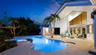Curved swimming pool with integrated spa and tiled accents, expansive patio with concrete surfacing, and tropical landscaping