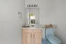 Vanity with a light wood-finish cabinet and stone-look countertop, a large wall-mounted mirror, and a four-bulb vanity light fixture