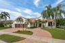 White stucco exterior with a terra cotta tile roof, a curved paver driveway, a two-car garage with wood-look doors, and lush landscaping